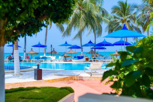 a pool with blue umbrellas and chairs and the ocean at Hôtel AFRICA QUEEN in Somone