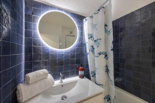 La salle de bains est pourvue de carrelage bleu, d'un lavabo et d'un miroir. dans l'établissement L'Océane - Joli studio avec balcon à Arcachon, à Arcachon