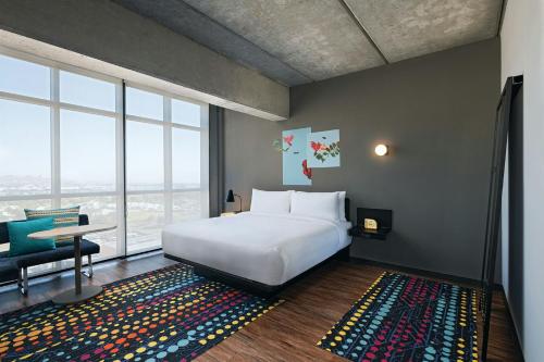 a bedroom with a white bed and a desk and window at Aloft Guadalajara Sur in Guadalajara