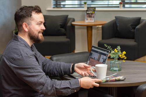 a man sitting at a table with a laptop at HQ Aparthotel Farnborough in Farnborough