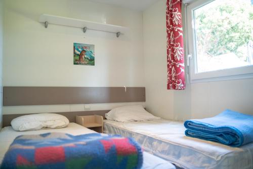 two twin beds in a room with a window at Camping écovillage Soleil du Pibeste in Agos-Vidalos