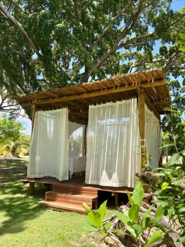 a wooden cabin with white curtains in the grass at Angá Beach Hotel in São Miguel dos Milagres