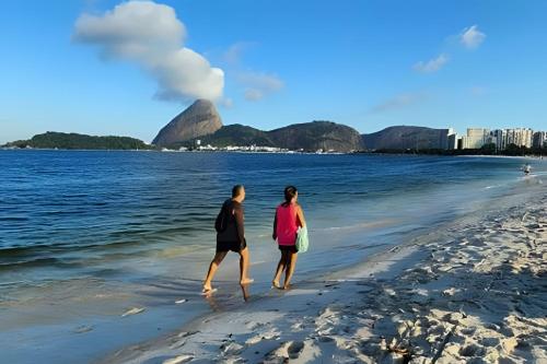 two people walking on the beach near the water at Chic retrô no Flamengo in Rio de Janeiro