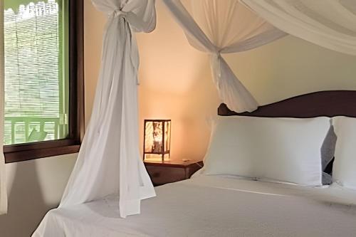 a bedroom with a bed with white sheets and a window at Licuri Praia de Algodões à poucos passos do mar. in Marau