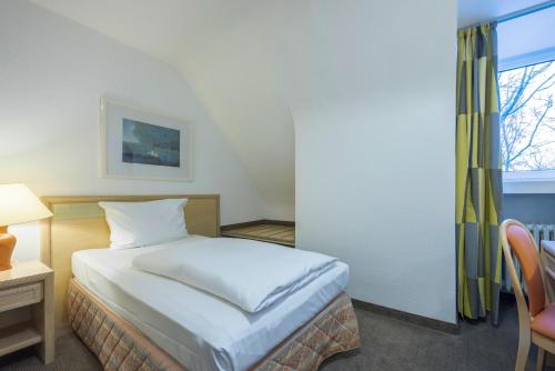 a bedroom with a bed and a desk and a window at Fletcher Waldhotel Nordrhein-Westfalen in Heiligenhaus