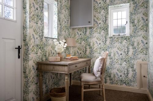 een bureau met een lamp en een stoel in een kamer met behang bij Broadway Country Chic Cottage in Broadway