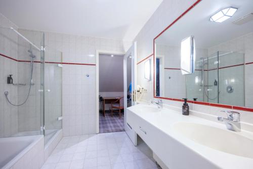 a white bathroom with two sinks and a shower at Fletcher Waldhotel Nordrhein-Westfalen in Heiligenhaus