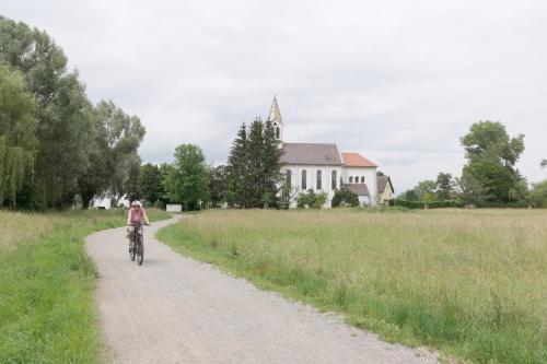 a person riding a bike down a dirt road in front of a church at Ferienwohnung, 2 Zimmer, 4 bis 6 Personen, 67 qm, mit großem Balkon, entlang am Fluss, an der Aach, am Bodensee, nah am Naturschutzgebiet in Singen