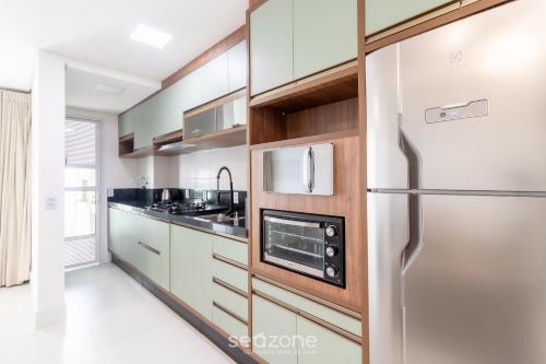 a kitchen with white cabinets and a stainless steel refrigerator at Condomínio a beira-mar c/ piscina - SHC in Piçarras
