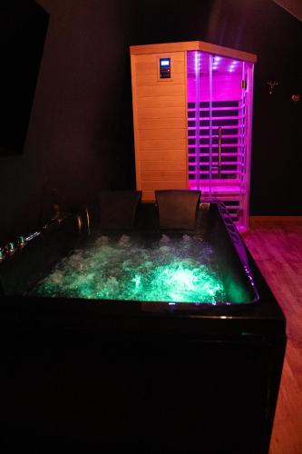 a hot tub in a room with purple and green lights at Love Room AMeuse&Vous in Hastière-par-delà