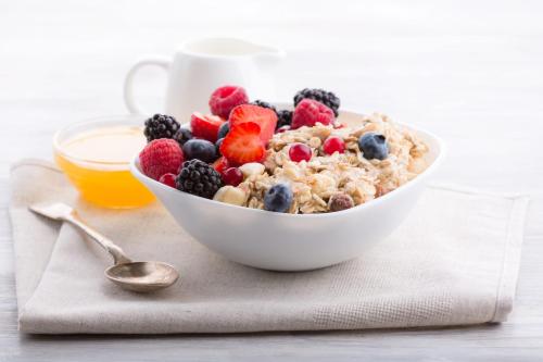 a bowl of cereal with berries and a cup of orange juice at Plitvice Falls Cottage in Plitvica selo