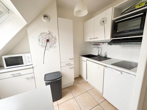 a kitchen with white cabinets and a dandelion drawing on the wall at Les diablotines - 6 couchages 2 sdb - proche plage in Cabourg