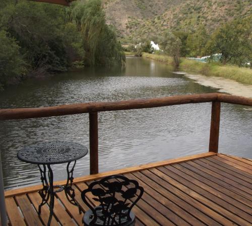 a table on a deck with a view of a river at Old Mill Lodge, Seasonal Working Ostrich Farm & Restaurant, Oudtshoorn in Oudtshoorn