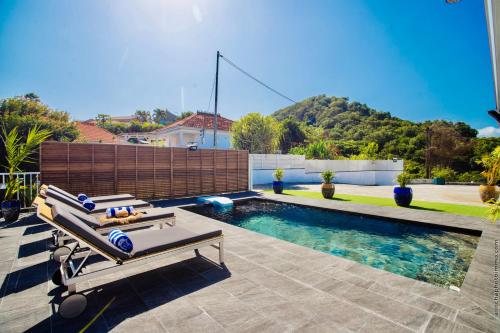 a swimming pool with two benches in front of a house at Villa Tropic Hirondelle - Piscine Vue Mer in Le François