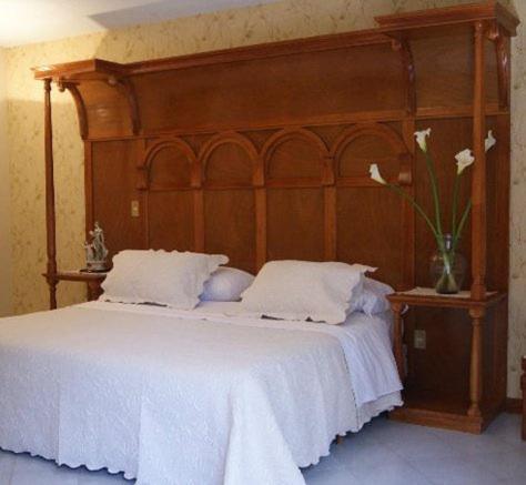 Una cama con cabecero de madera y un jarrón con flores en Quintaesencia Hotel Boutique, en Huasca de Ocampo