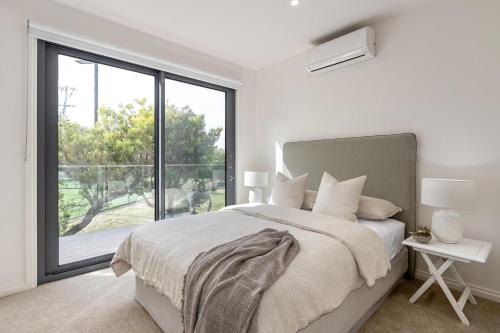 a white bedroom with a bed and a large window at Back Beach in Portsea