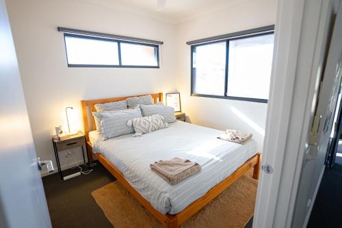 a bedroom with a bed with white sheets and two windows at Suburban Sanctuary South Hedland in South Hedland