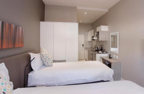 a bedroom with two white beds and a kitchen at The Capital on Bath in Johannesburg