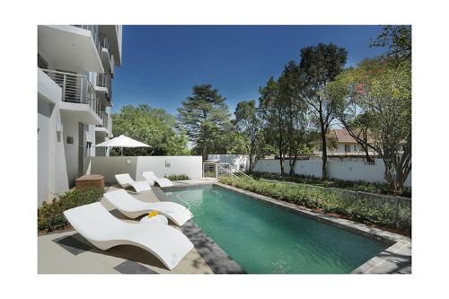 a swimming pool with white chairs next to a building at The Capital on Bath in Johannesburg