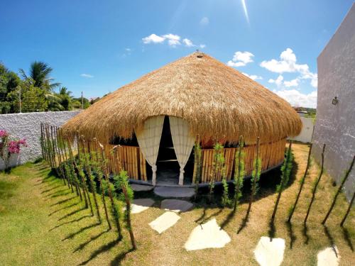 a large hut with a grass roof with plants at Oasis Tajaja Pousada in Jacumã