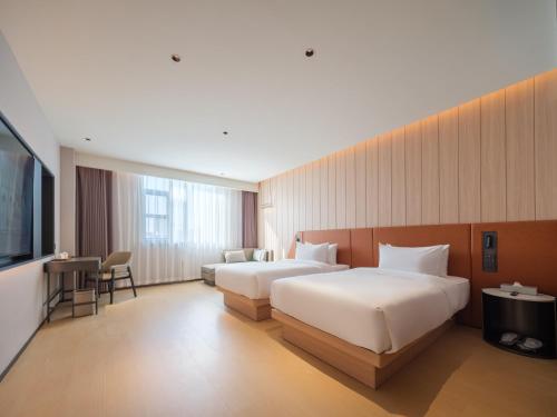 a hotel room with two beds and a flat screen tv at 桔作酒店 郑州中州大道中原国际博览中心店 in Zhengzhou