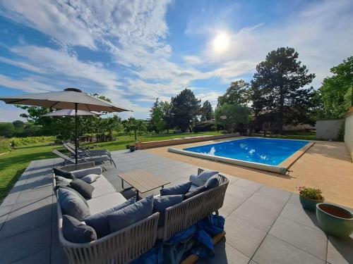 une terrasse avec des canapés, un parasol et une piscine dans l'établissement Charmant gîte de 4 à 6 personnes à 5km de Duras, à Savignac-de-Duras