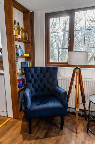 a blue chair in a living room with a window at Heron's Perch- A pond-side retreat with cinema room in Callington