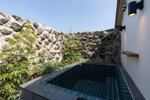 a bathroom with a green tile floor next to a stone wall at HacheonBaramJip Angeori Stay Curated by Actor Ryu Seungryong in Jeju