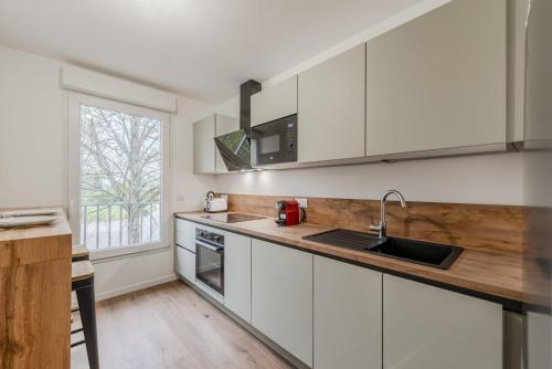 une cuisine avec des armoires blanches, un évier et une fenêtre dans l'établissement OIQIA • Palmeraie, à Bussy-Saint-Georges