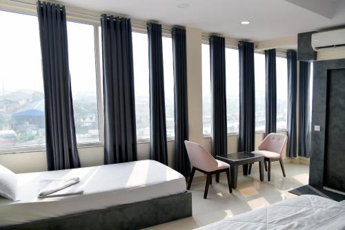 a bedroom with a bed and chairs and windows at Hotel M Plaza Dhulagarh in Dhulagari