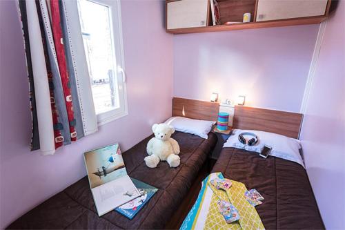 - une petite chambre avec un ours en peluche assis sur un lit dans l'établissement Mobil Home 2 chambre 4 à 6 personne en camping 4 étoiles, à Torreilles