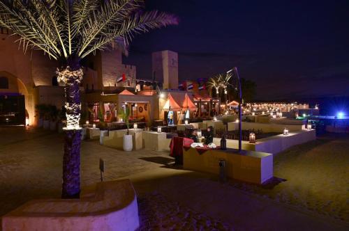 a group of tables and palm trees at night at Arobab desert safaris in Ajman 