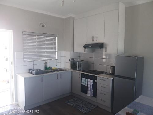 Una cocina con gabinetes blancos y un refrigerador. en Muizenberg Magic OceanfrontOasis, en Marina da Gama