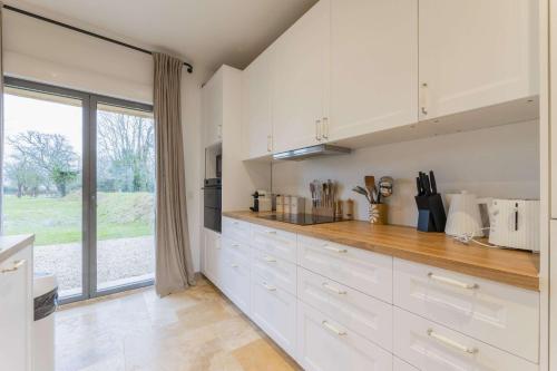 une cuisine avec des placards blancs et une grande fenêtre dans l'établissement Maison des Pommiers Elegant house near Deauville, à Cricquebœuf