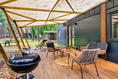 a outdoor patio with a grill and chairs and a smoker at Cozy Chalet w terrace in the Middle of the Forest in Veluwe in Doornspijk