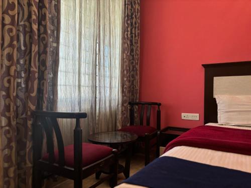 a room with a bed and a window and chairs at Golden Larch Comfort in Ooty