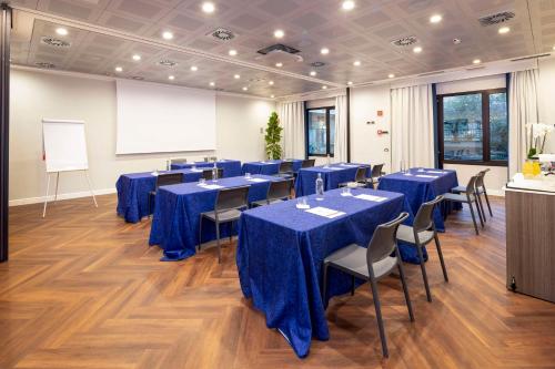 a conference room with blue tables and chairs and a whiteboard at Best Western Plus Borgolecco Hotel in Arcore