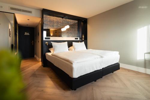a bedroom with a bed with white sheets and a window at Van der Valk TheaterHotel De Oranjerie in Roermond