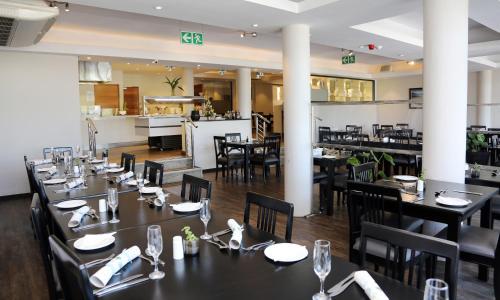 a restaurant with black tables and chairs and a kitchen at Blue Lagoon Hotel and Conference Centre in East London
