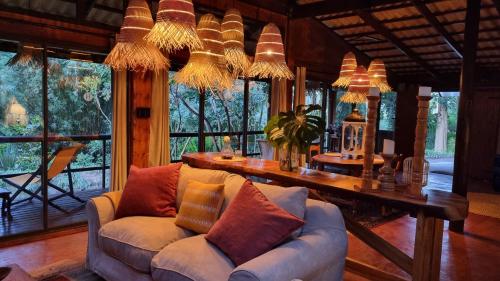 a living room with a couch and a table and windows at Honeywood Forest Lodge in Port Shepstone