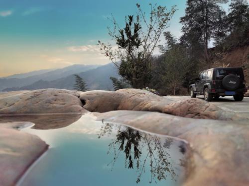 a jeep driving down a road with a reflection in the water at Longji Skyreach Peak Resort - Golden Buddha Summit in Longsheng