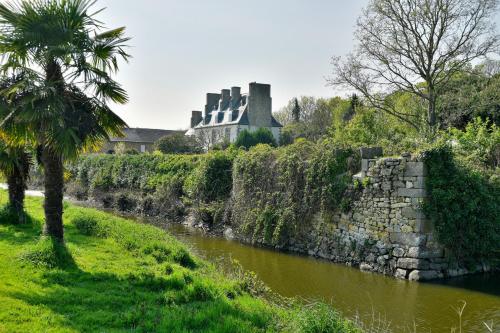 un mur de pierre à côté d'une rivière avec un château en arrière-plan dans l'établissement Domaine de Launay blot, à Baguer-Morvan