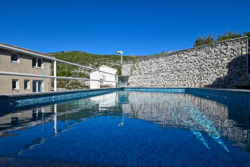 a swimming pool in front of a stone wall at Apartments Marić in Primošten