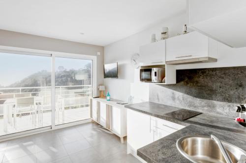 une cuisine avec des placards blancs et une grande fenêtre dans l'établissement Studio Bougainvillier - Welkeys, à Cavalaire-sur-Mer