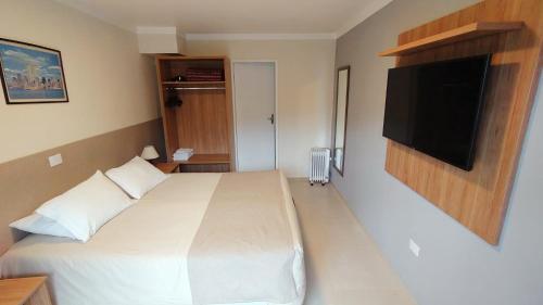 a bedroom with a white bed and a flat screen tv at Village de Charme - 2km do Capivari in Campos do Jordão