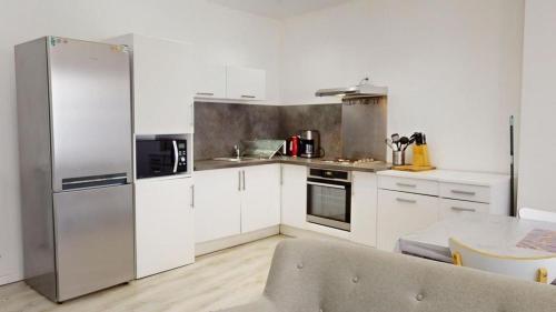 une cuisine avec des armoires blanches et un réfrigérateur en acier inoxydable dans l'établissement Le Stéphanois cozy centre-ville spacieux, à Saint-Étienne