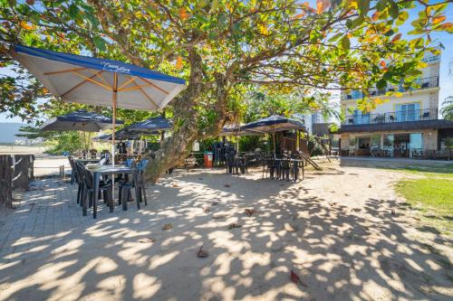 a table and chairs under a tree with umbrellas at Pousada Conca di Mare - Restaurante - Pé na areia in Bertioga