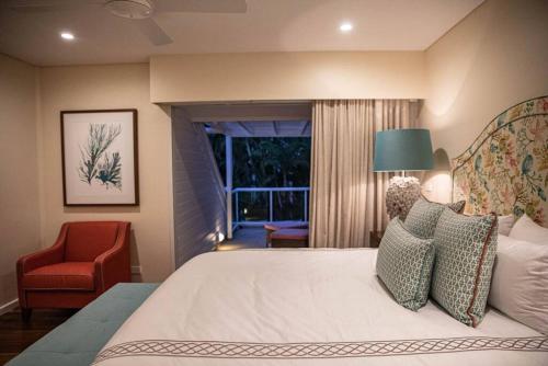 a bedroom with a bed and a chair and a window at Villa 437 Coral Shore Villa in Port Douglas