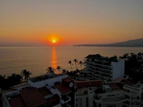 a sunset over the ocean with buildings and palm trees at LIFE Bucerias Zona Dorada Tranquil Beach Loft in Bucerías