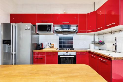 une cuisine équipée de placards rouges et d'appareils en acier inoxydable dans l'établissement Grande maison 3 chambres calme 35 min de Paris Centre, à Romainville